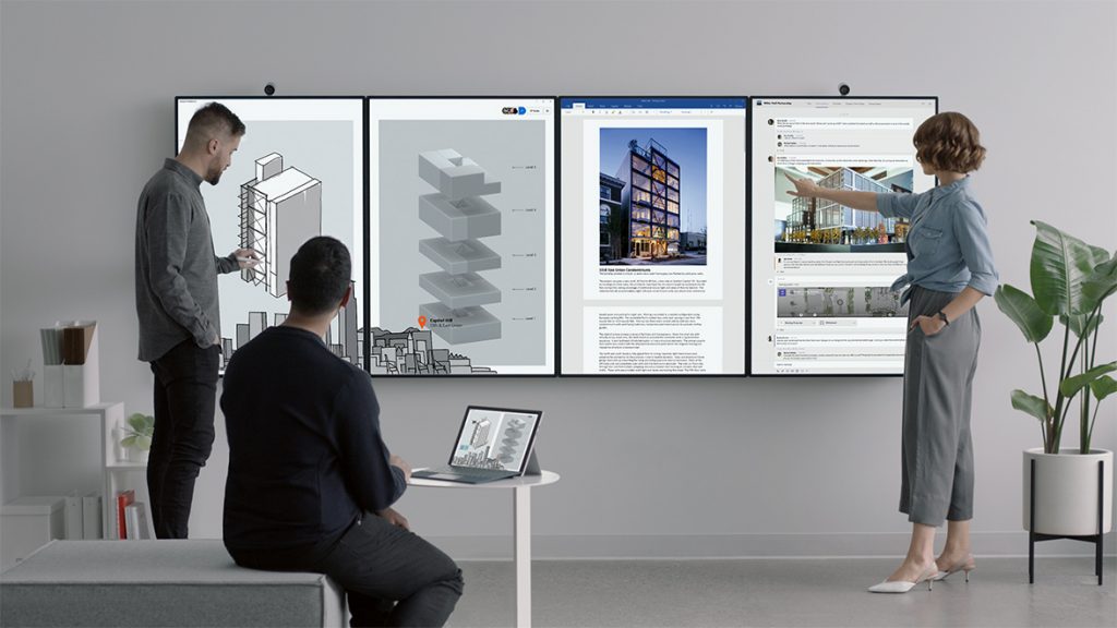 Three people working with four Surface Hub 2 displays